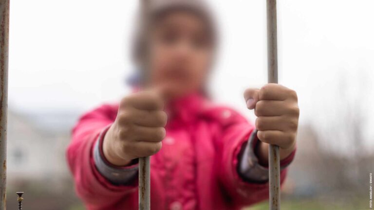Little girl behind bars. Concept of homeless children. Child captivity. Sad child