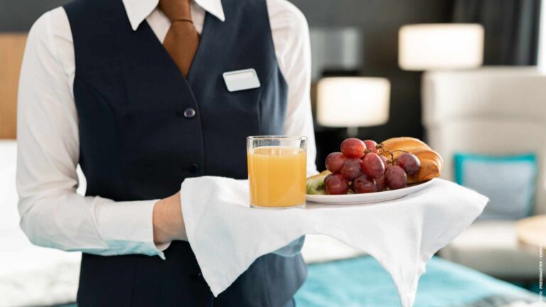 Midsection of young elegant female worker of hotel holding tray with breakfast