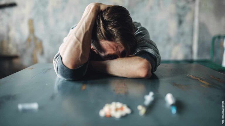 Male junkie at the table with drugs and syringe