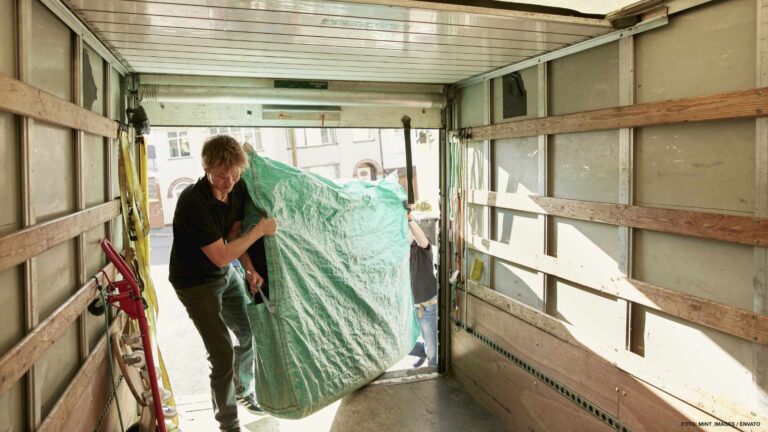 Removals business. A man lifting an item of furniture covered in green plastic into a removals van. ,Moving Home with Removals Company,United Kingdom