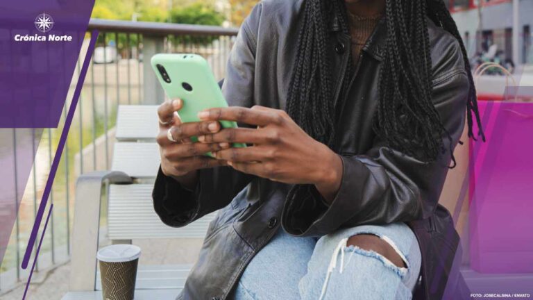 Happy teenage african american girl smiling doing shopping online with a cellphone sitting on a bench outdoors. Young woman with braids and hipster clothing texting using a smart phone at city street. Communication concept.