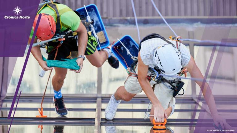 Industrial mountaineering worker cleaning window outside building.